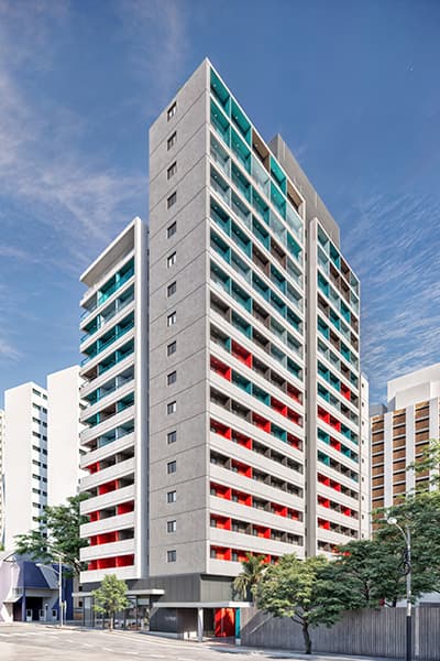 Fachada externa do edifício com detalhes coloridos nas varandas e arborização.
