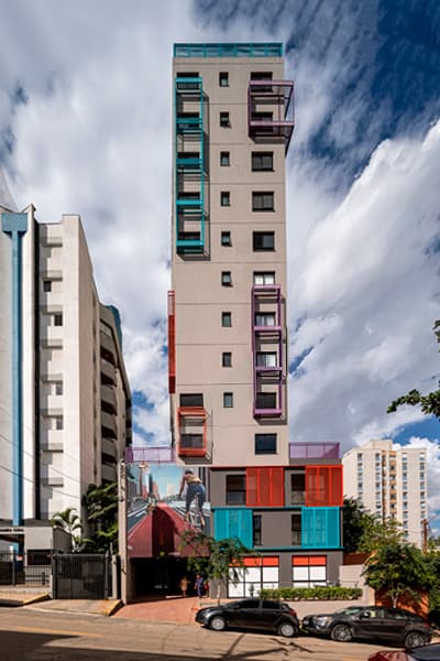 Fachada do edifício alto com detalhes coloridos e carros estacionados na rua.