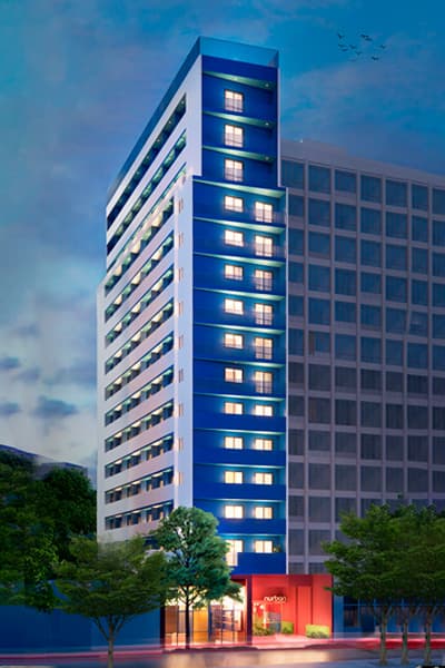Fachada de edifício residencial iluminada ao entardecer com fachada azul e branca.