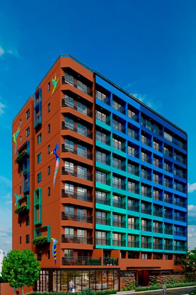 Fachada lateral de edifício residencial colorido em tons de laranja, azul e verde, com varandas e térreo comercial